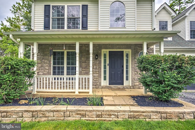 view of exterior entry with stone siding and a porch