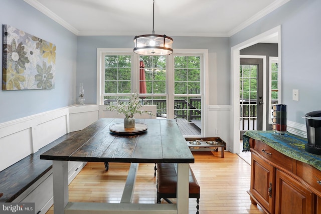 dining room with ornamental molding, light wood-style floors, and a wainscoted wall