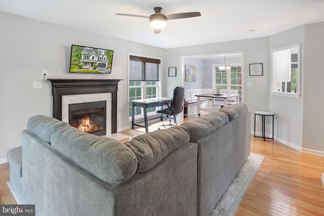 living area with baseboards, a premium fireplace, light wood-style flooring, and ceiling fan