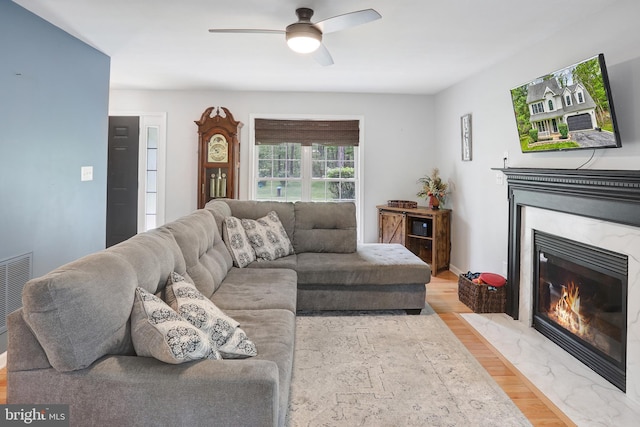living area featuring a premium fireplace, light wood finished floors, a ceiling fan, and visible vents