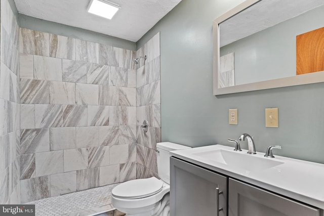 bathroom with toilet, tiled shower, and vanity