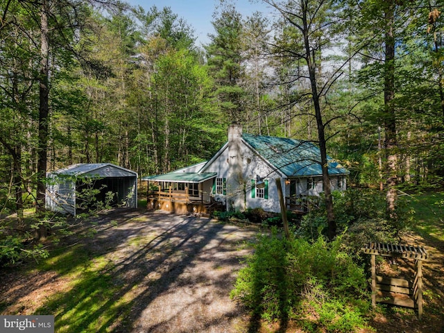 view of front of home featuring a chimney, a view of trees, metal roof, dirt driveway, and a carport