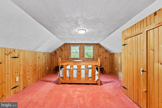 unfurnished bedroom featuring vaulted ceiling, a textured ceiling, carpet floors, and wooden walls