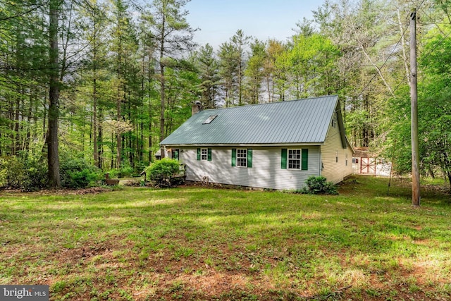 view of side of home featuring metal roof, a lawn, a chimney, and a wooded view