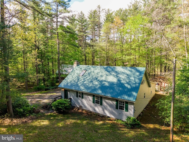 view of property exterior with metal roof, a chimney, and a view of trees