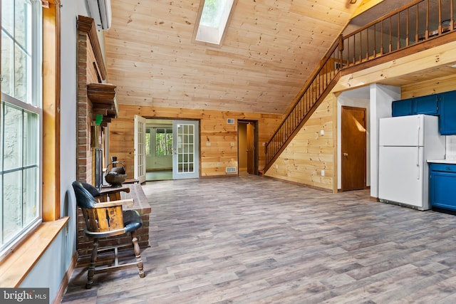 interior space with wooden walls, a skylight, wood finished floors, high vaulted ceiling, and stairs