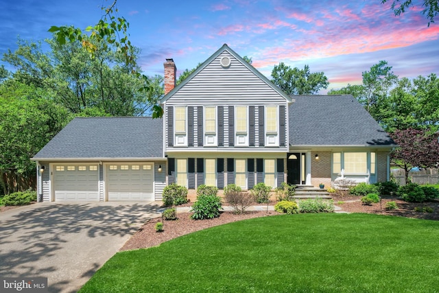 view of front of property with an attached garage, a chimney, driveway, a lawn, and a shingled roof