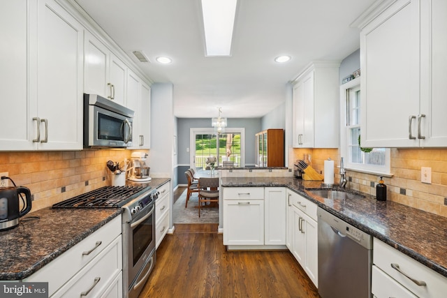 kitchen with stainless steel appliances, a sink, dark wood-type flooring, white cabinets, and a peninsula
