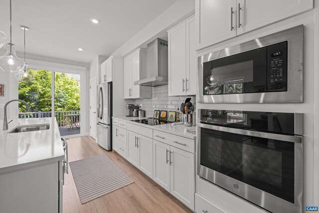 kitchen featuring a sink, stainless steel appliances, wall chimney exhaust hood, white cabinetry, and light countertops