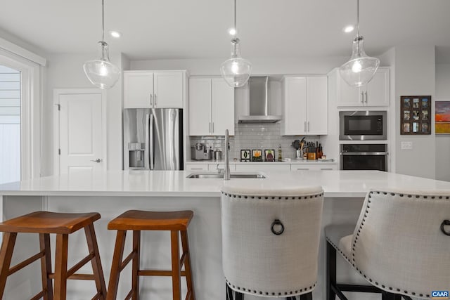 kitchen with a sink, wall chimney exhaust hood, light countertops, appliances with stainless steel finishes, and tasteful backsplash