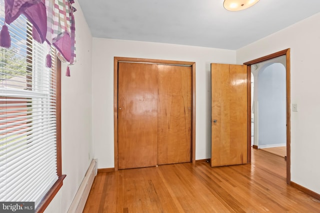 unfurnished bedroom with a baseboard radiator, light wood-type flooring, a closet, and baseboards