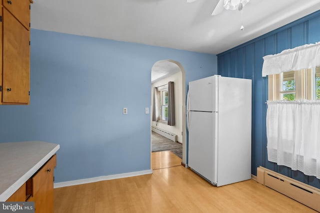 kitchen with freestanding refrigerator, baseboard heating, arched walkways, and light wood-type flooring