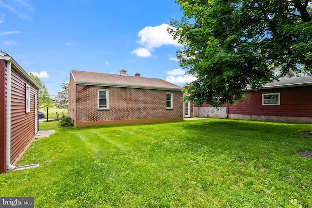 back of house featuring a yard, a chimney, and brick siding