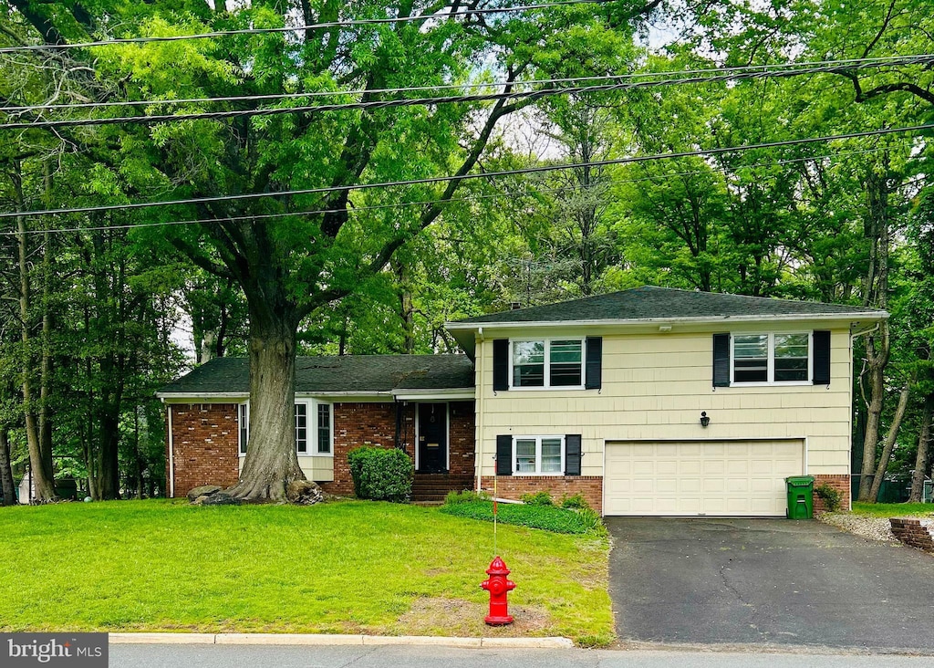 tri-level home with brick siding, driveway, an attached garage, a front yard, and a shingled roof