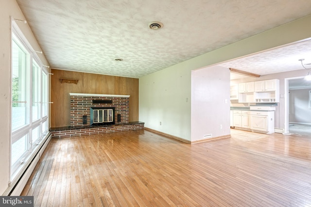407 Stately Dr, Pasadena, MD 21122 - unfurnished living room with baseboard heating, light wood-style floors, a textured ceiling, baseboards, and wooden walls