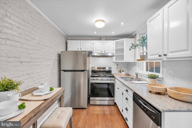 kitchen featuring stainless steel appliances, ornamental molding, under cabinet range hood, white cabinetry, and light stone countertops