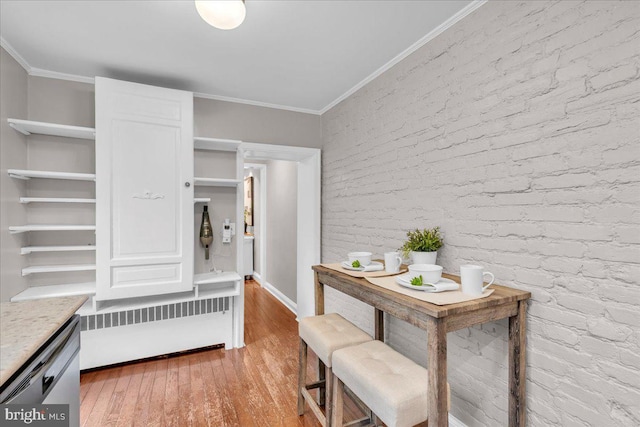 interior space with radiator, light wood-type flooring, ornamental molding, and brick wall