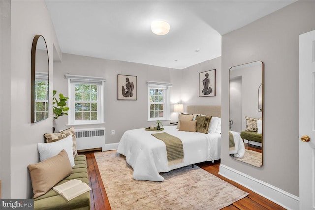 bedroom featuring wood finished floors, radiator, baseboards, and multiple windows
