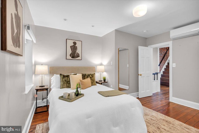 bedroom featuring a wall mounted air conditioner, baseboards, and wood-type flooring