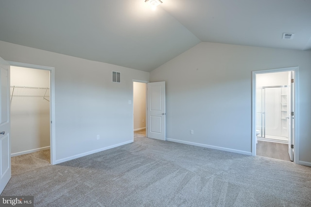 unfurnished bedroom featuring vaulted ceiling, carpet, visible vents, and a spacious closet