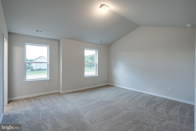 carpeted empty room with baseboards, visible vents, and vaulted ceiling