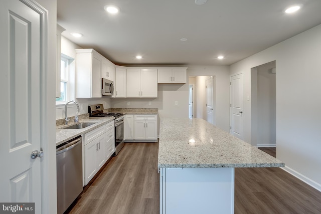 kitchen featuring light stone counters, a sink, a kitchen island, white cabinets, and appliances with stainless steel finishes