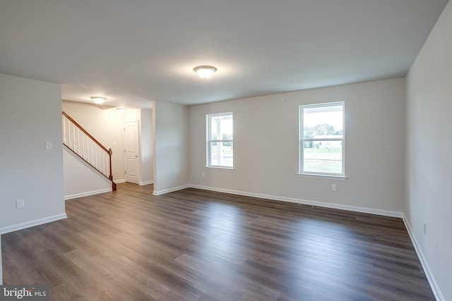 unfurnished living room featuring baseboards, dark wood-style flooring, and stairway