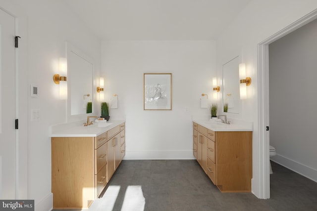 full bathroom featuring two vanities, baseboards, and toilet