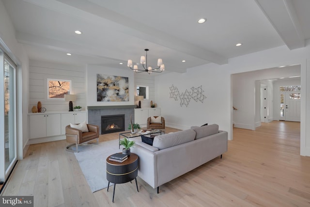 living room featuring beamed ceiling, light wood finished floors, a tile fireplace, a chandelier, and recessed lighting