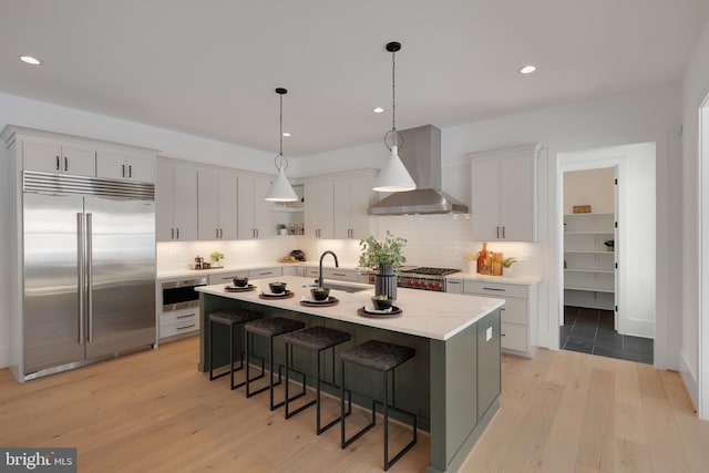 kitchen with appliances with stainless steel finishes, wall chimney range hood, light countertops, a breakfast bar, and backsplash