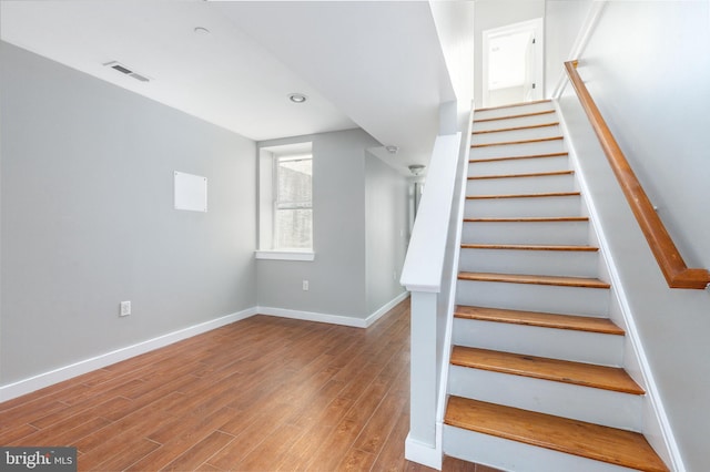 staircase with baseboards, visible vents, and wood finished floors