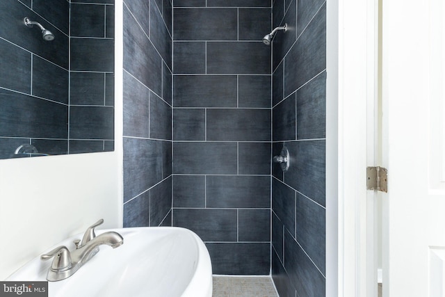 full bathroom featuring a tile shower and a sink