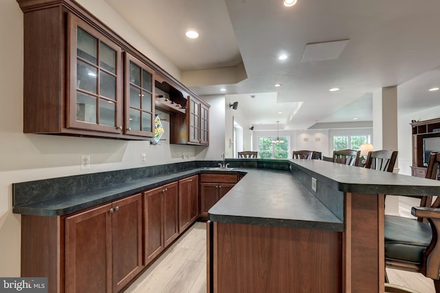 kitchen featuring dark countertops, a breakfast bar area, a peninsula, glass insert cabinets, and light wood-style floors