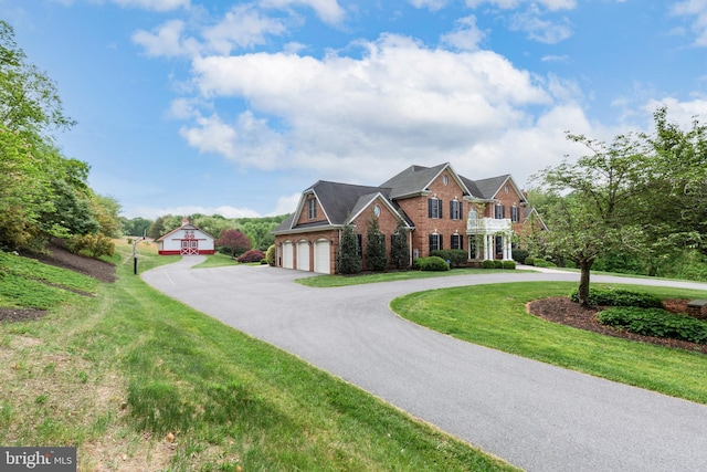 view of front of property featuring brick siding, curved driveway, a front lawn, and an outdoor structure