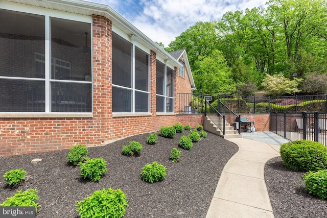 view of property exterior with brick siding, fence, and a sunroom