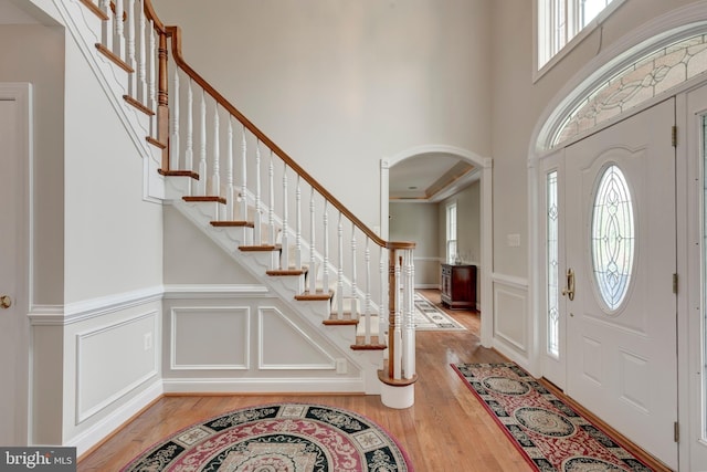 foyer entrance with plenty of natural light, light wood-style flooring, a decorative wall, arched walkways, and a wainscoted wall