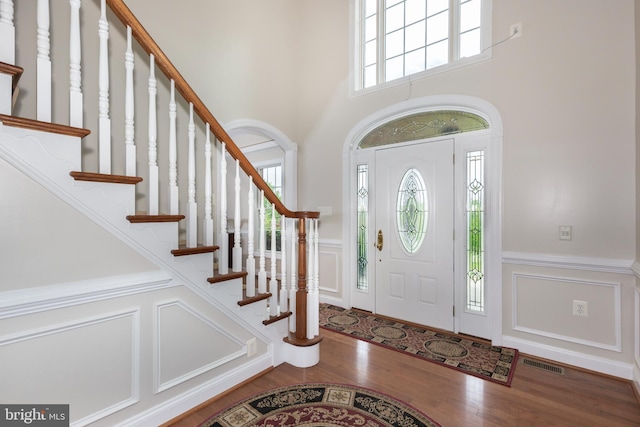 foyer entrance featuring a decorative wall, wainscoting, wood finished floors, stairs, and a towering ceiling