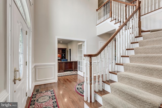 entrance foyer with stairway, hardwood / wood-style flooring, a high ceiling, and wainscoting