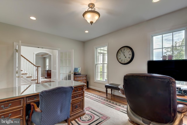 home office featuring healthy amount of natural light, recessed lighting, light wood-style flooring, arched walkways, and baseboards