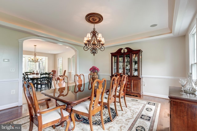 dining room featuring a chandelier, arched walkways, a tray ceiling, wood finished floors, and baseboards
