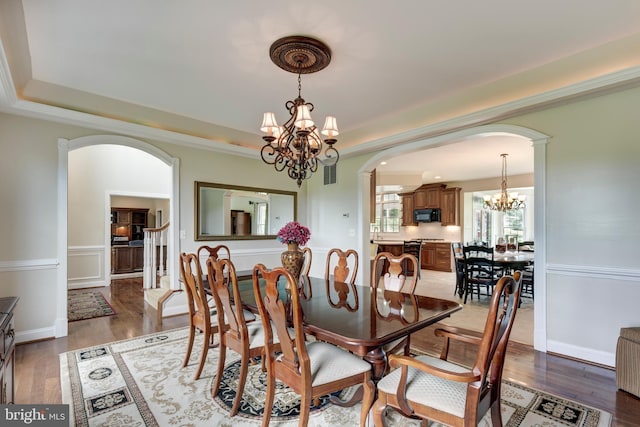 dining room featuring arched walkways, a chandelier, a tray ceiling, and light wood finished floors