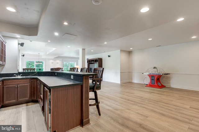 kitchen with a kitchen breakfast bar, dark countertops, light wood-style flooring, a sink, and recessed lighting
