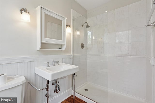 bathroom featuring a tile shower, toilet, and a wainscoted wall