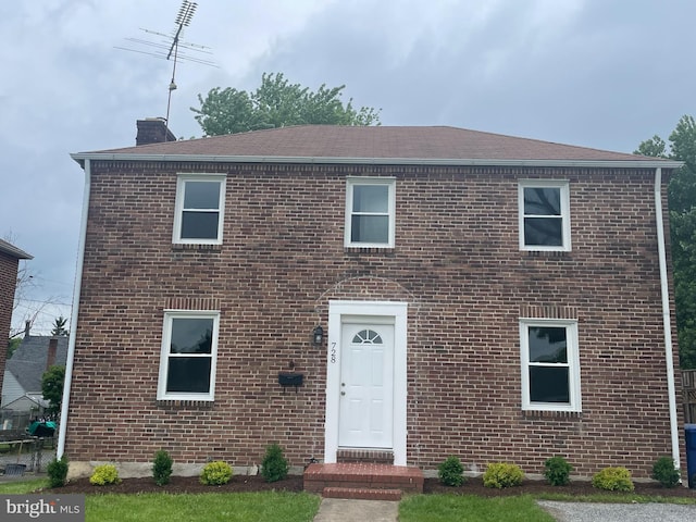 colonial-style house featuring brick siding, roof with shingles, and a chimney