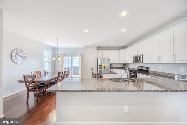 kitchen featuring appliances with stainless steel finishes, a sink, white cabinets, light stone countertops, and a peninsula