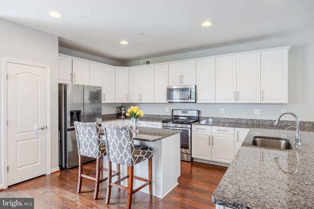kitchen with stainless steel appliances, a sink, stone counters, white cabinets, and a kitchen breakfast bar