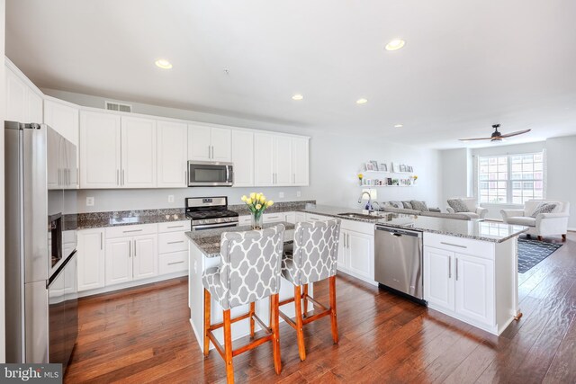 kitchen with stainless steel appliances, a peninsula, a sink, open floor plan, and white cabinets