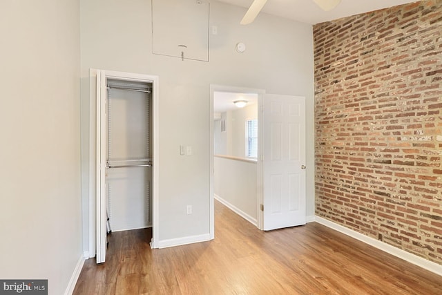 unfurnished bedroom featuring brick wall, wood finished floors, baseboards, a towering ceiling, and a closet