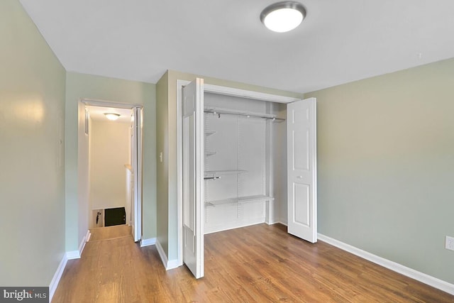 unfurnished bedroom featuring wood finished floors, baseboards, and a closet