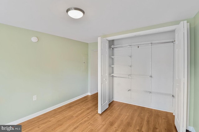 unfurnished bedroom featuring wood finished floors, baseboards, and a closet